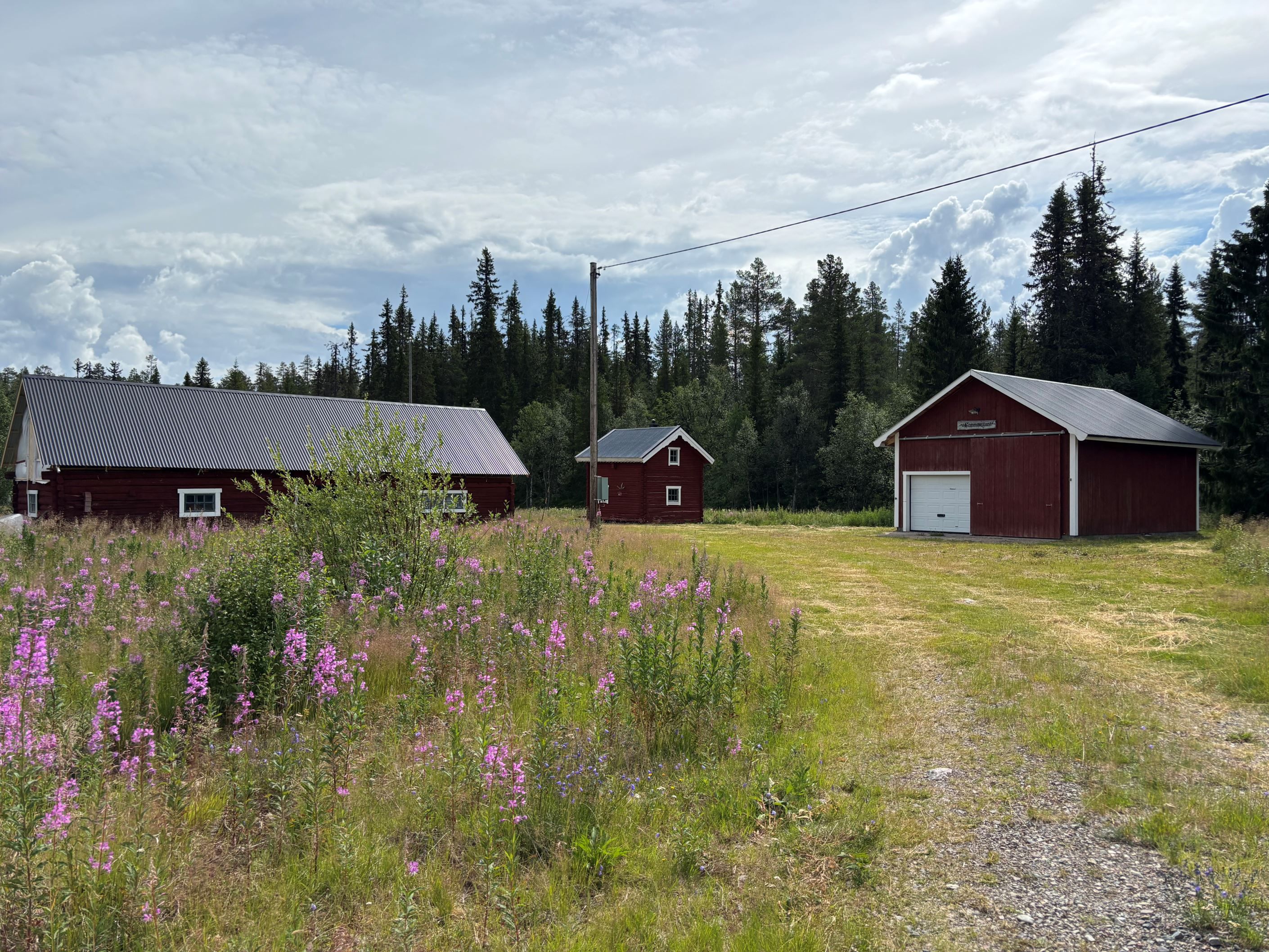Gården sett från infarten med garage t.h och ladan t.v i bild