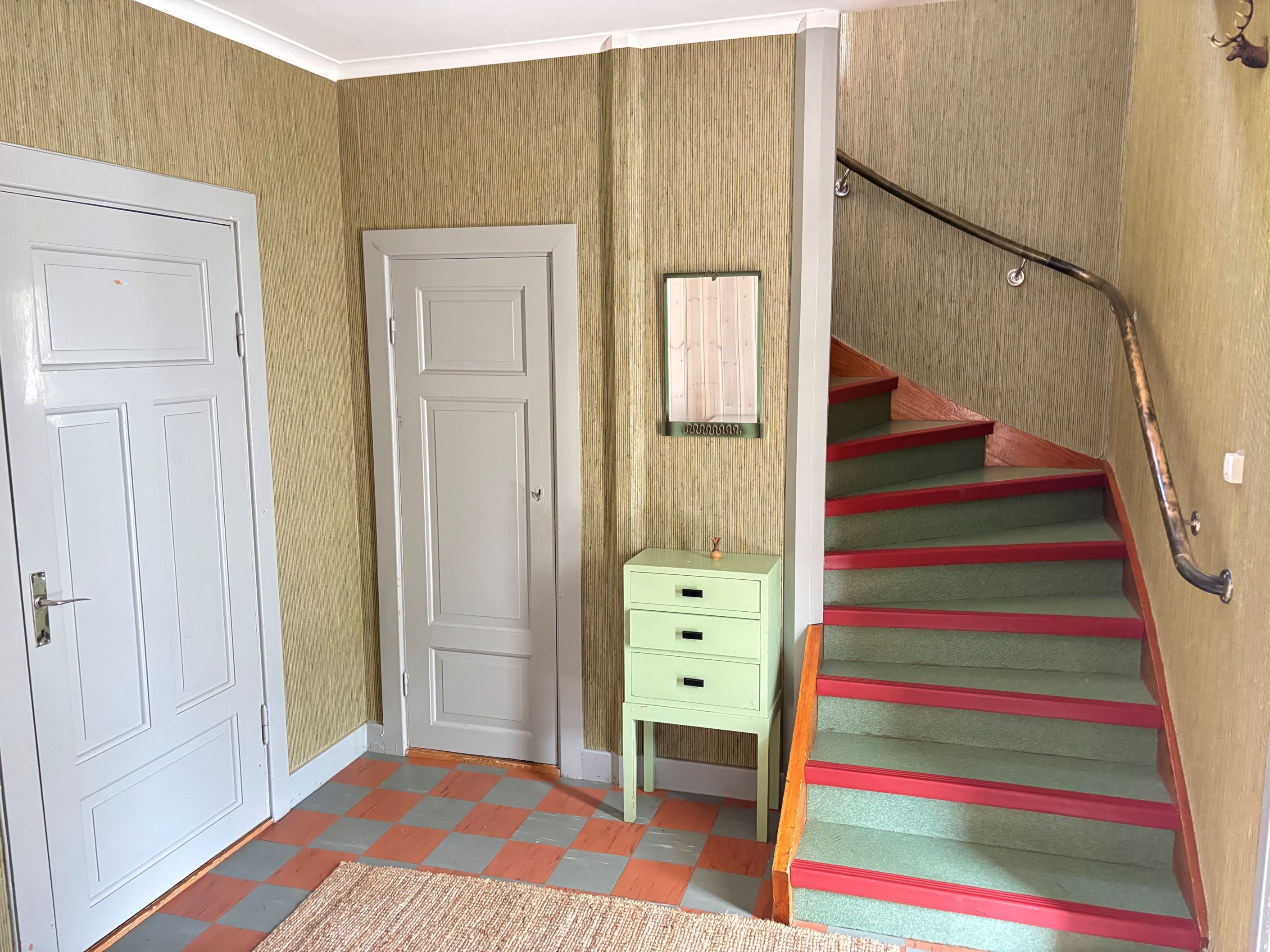 Hall med allrum t.v i bild och dörr till källare rakt fram i bild