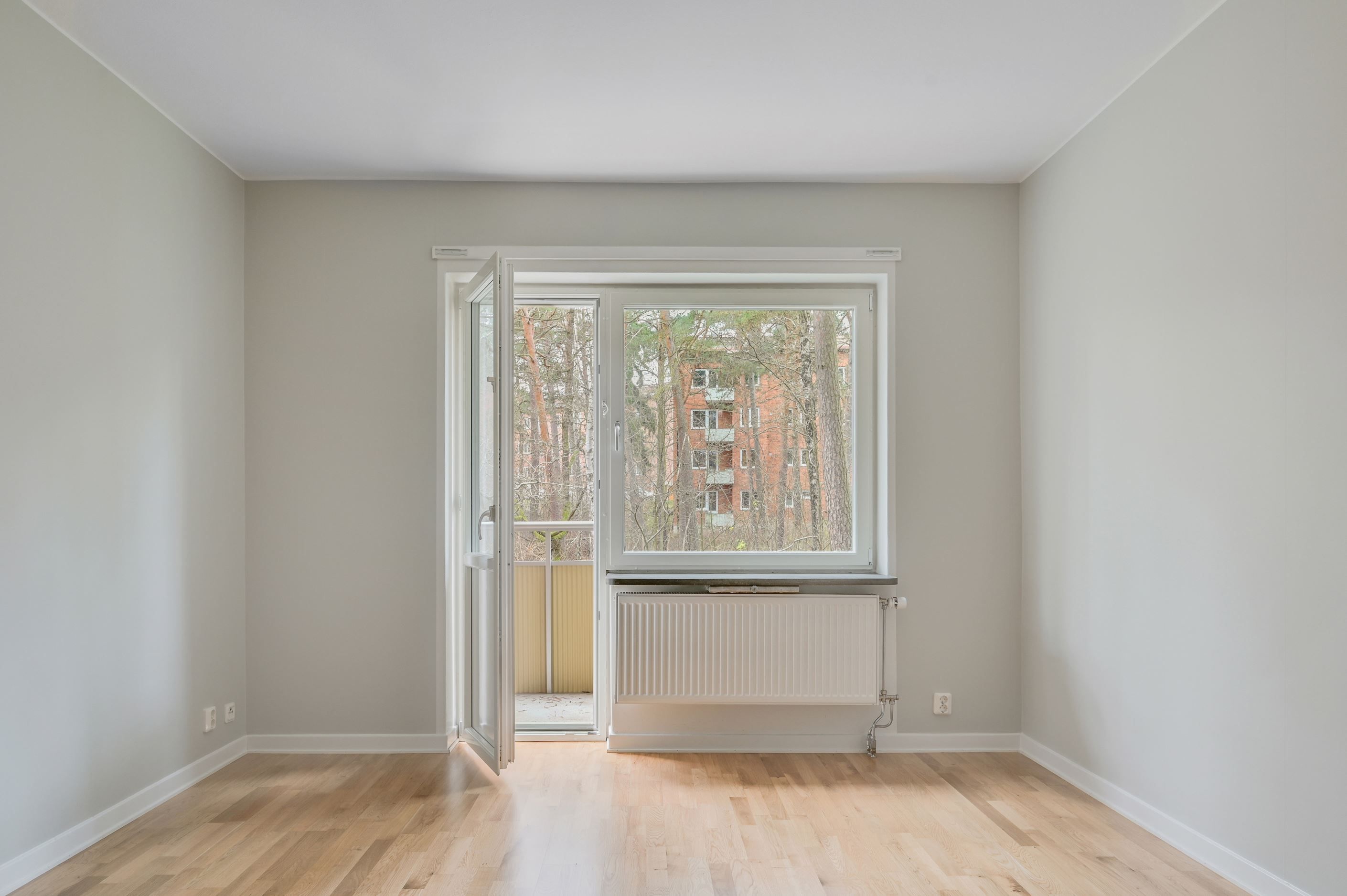 Stora fönster mot skogsparti och utgång till balkong från vardagsrummet