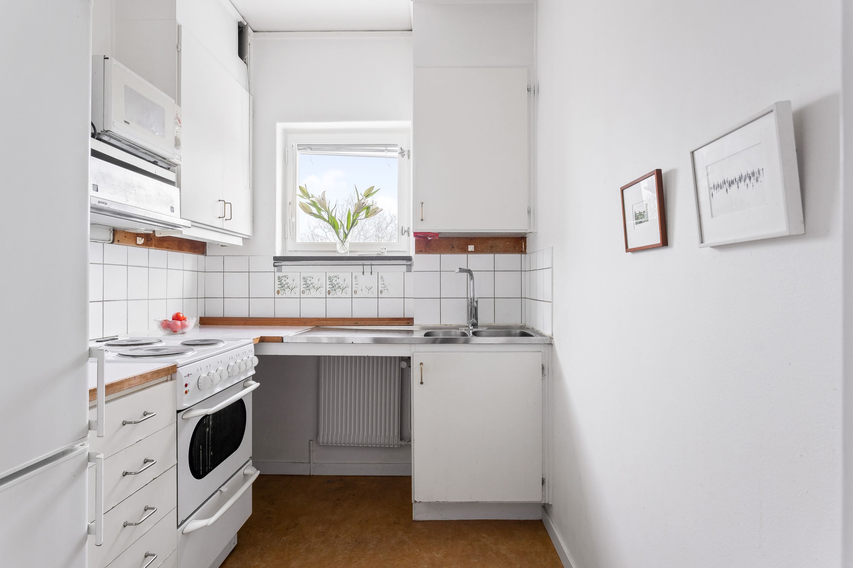 Kök med vita snickerier och utsikt över lummigt grönområde