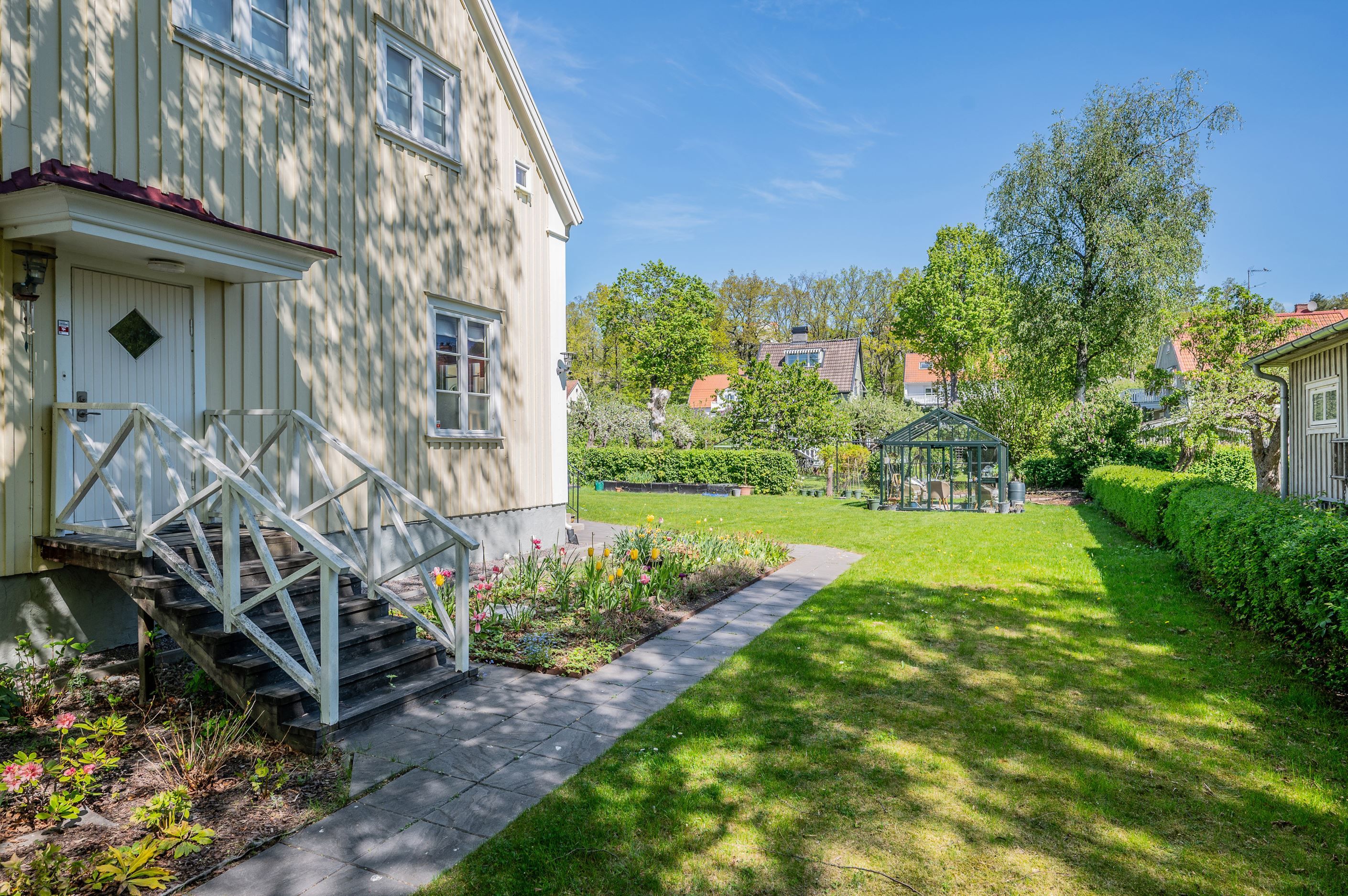 Fint anlagd tomt med smaragdgrön gräsmatta och stensatta gångar runt huset