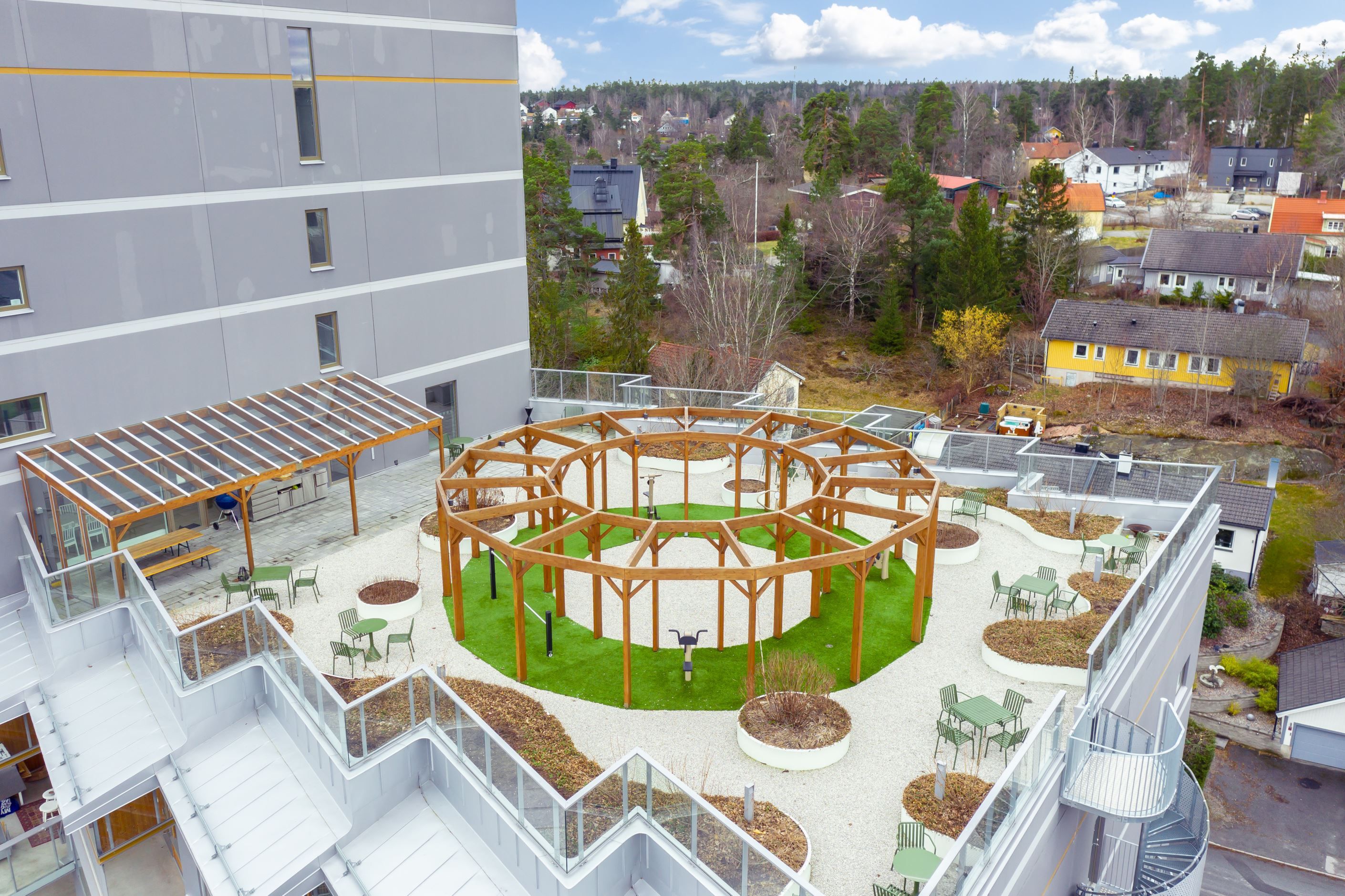 Terrass med sittmöbler, matgrupp, grill, gym och ingång till gemensamhetslokal.