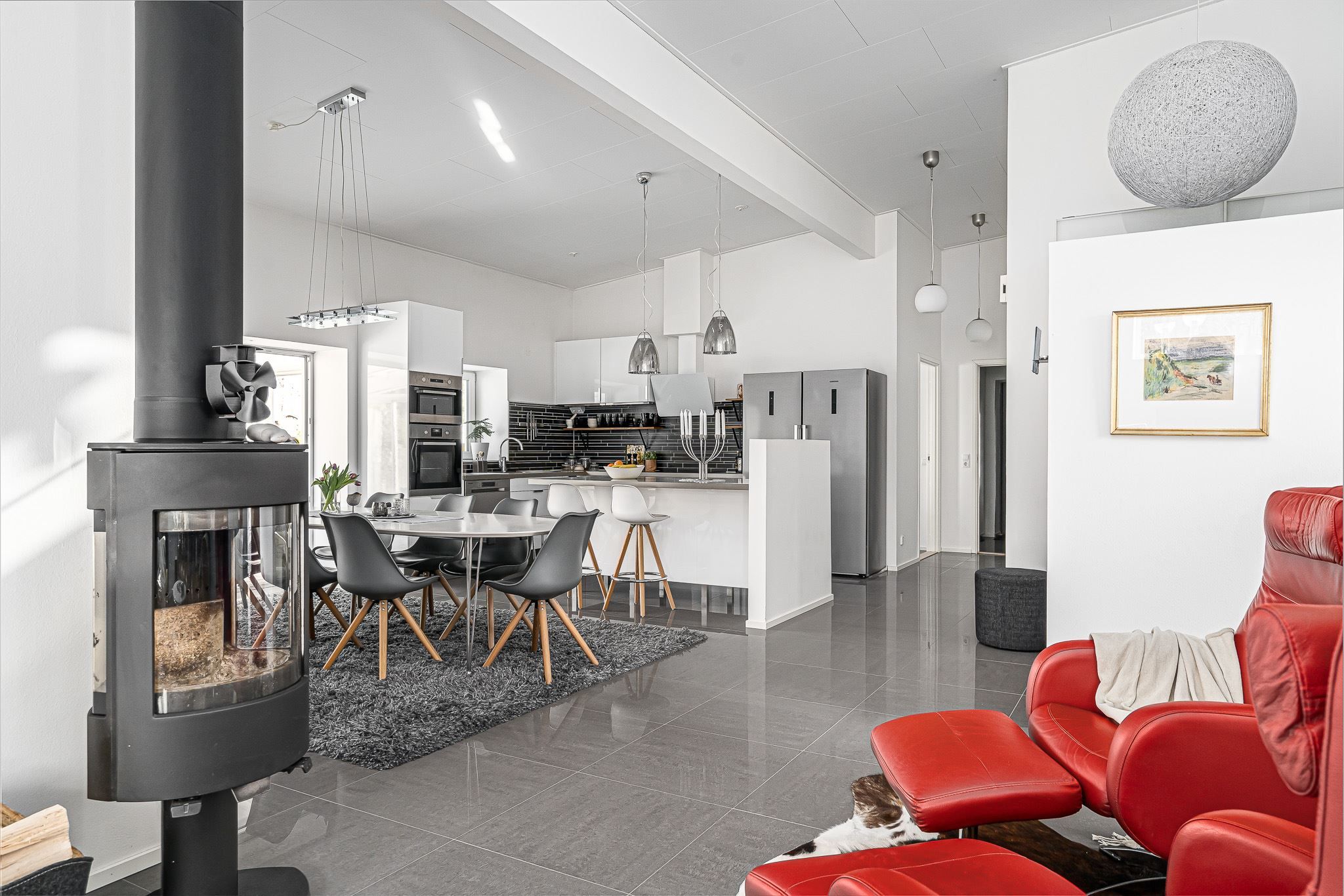 Öppen planlösning mellan kök och vardagsrum med värmande kamin centralt placerad