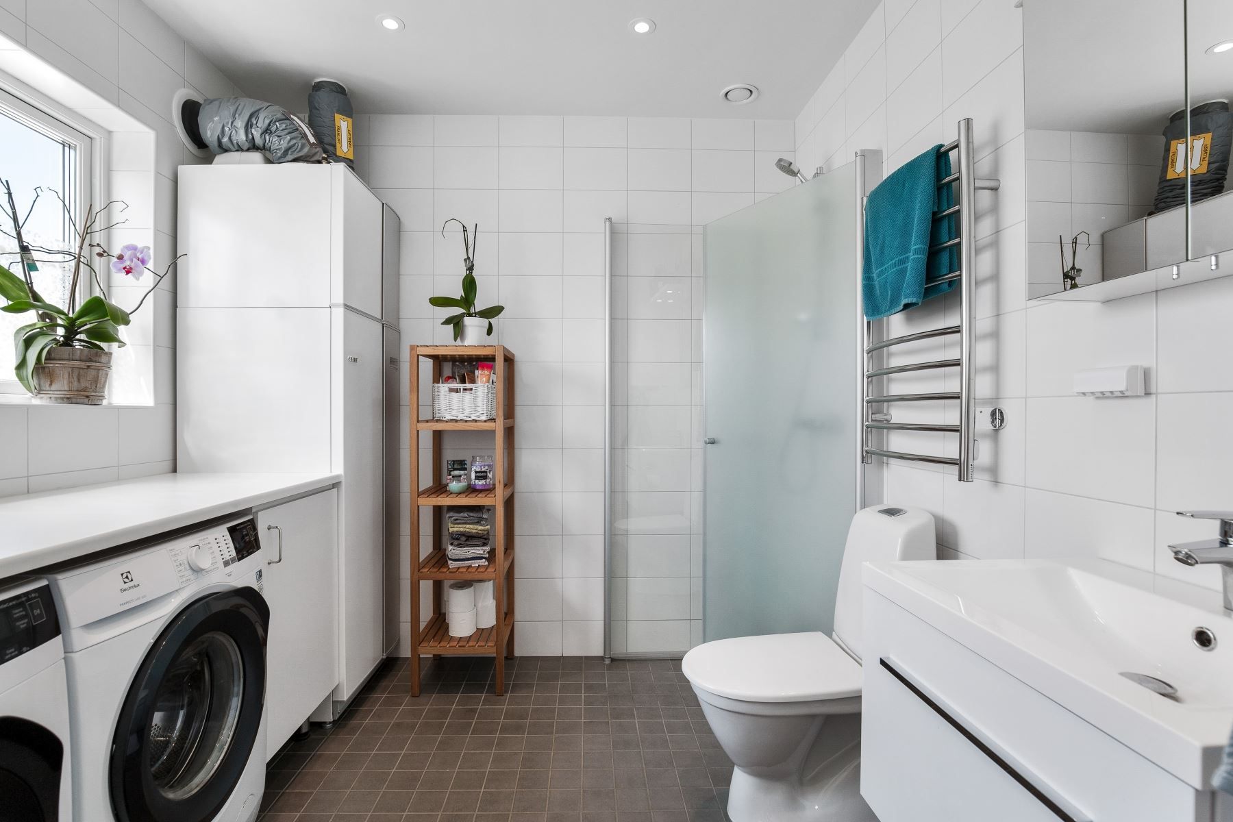 Helkaklat badrum med duschvägg, handdukstork och tvättmaskin och torktumlare.