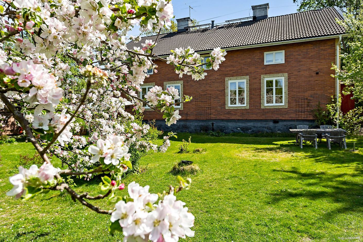 Prunkande trädgård åt väst med stora gemensamma gräsytor, buskage och planteringar