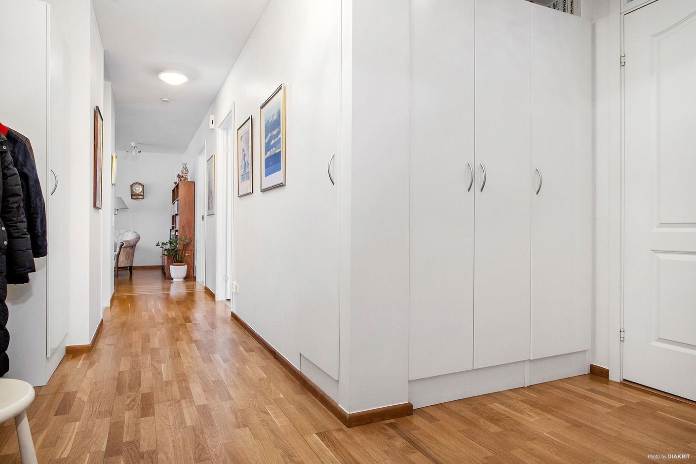 Stor hall med garderober. På rad ligger badrum, två sovrum, kök och vardagsrum längst bort i hallen