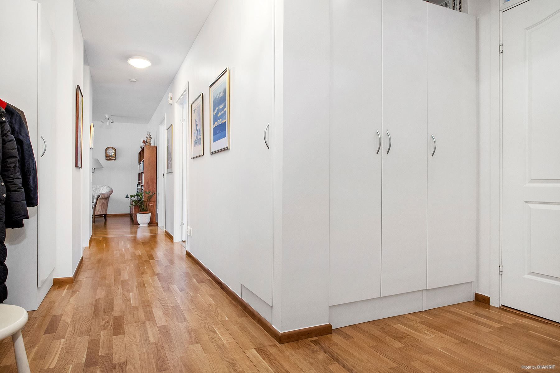 Stor hall med garderober. På rad ligger badrum, två sovrum, kök och vardagsrum längst bort i hallen