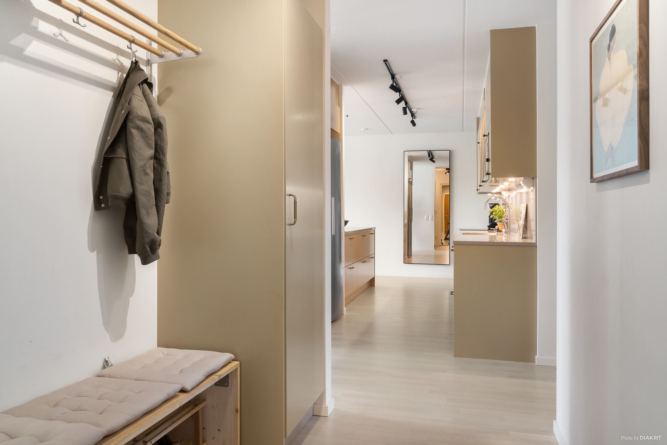 Välkomnande hall med hatthylla samt garderob i samma vackra havregula färg som inredningen i köket